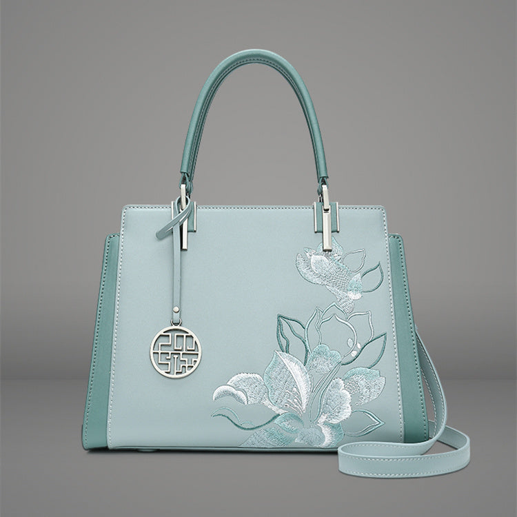 Light blue handbag with floral embroidery on a gray background