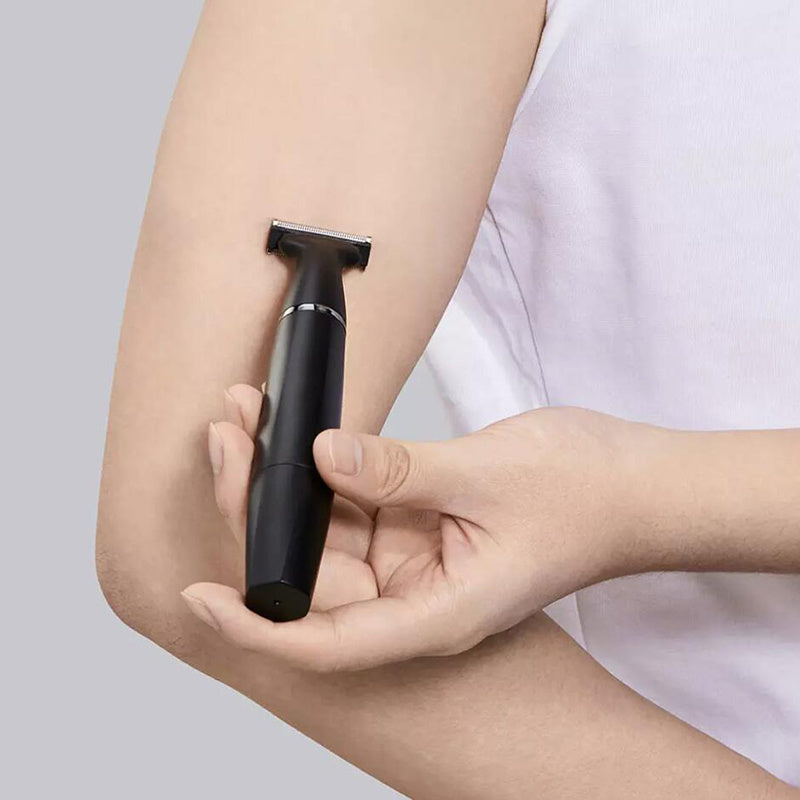 Person holding a black electric razor against their arm on a light gray background