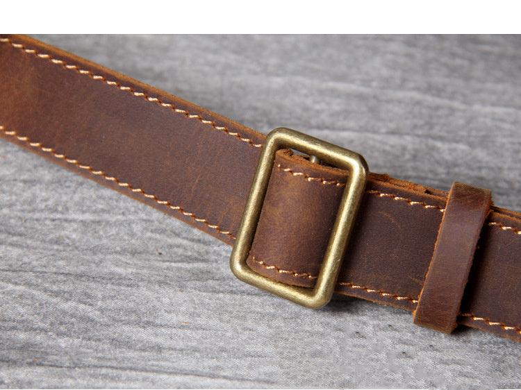 Brown leather belt with a brass buckle on a gray background