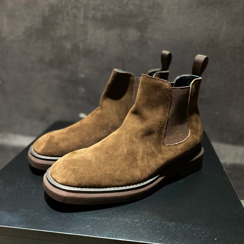 Pair of brown suede Chelsea boots on a dark surface with a gray background