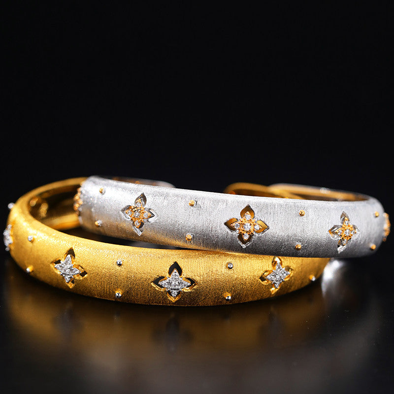 Two gold bracelets with star and flower designs on a dark background