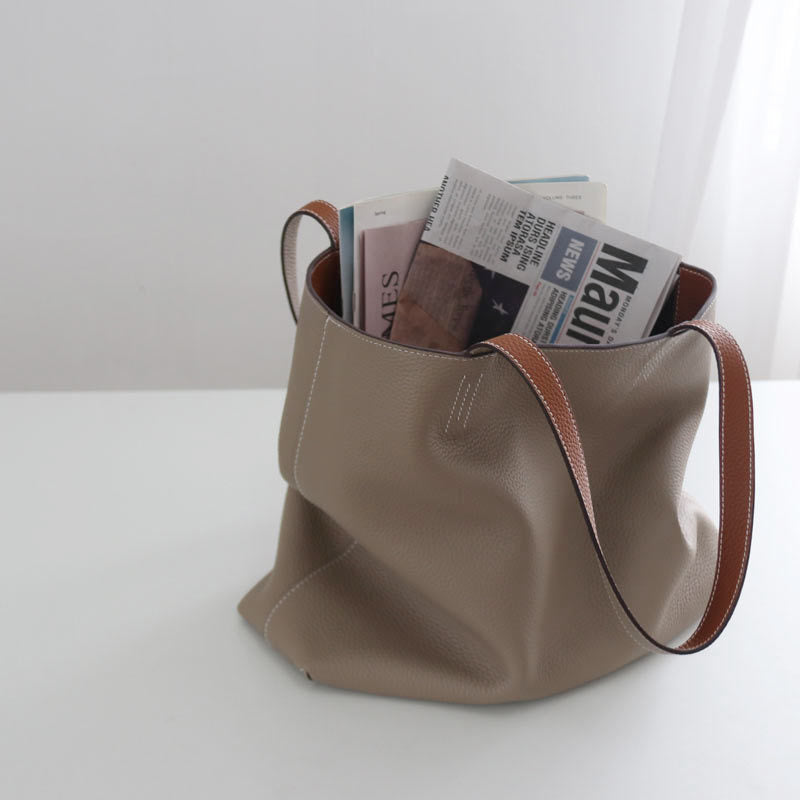Beige handbag with brown handles filled with newspapers on a white surface.