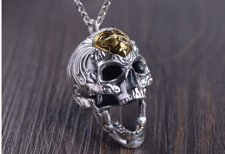 Skull-shaped pendant with gold and silver details on a wooden surface