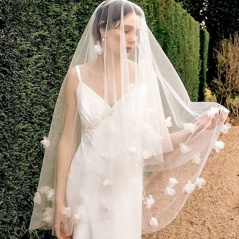 Woman wearing a white wedding dress with a floral veil outdoors.
