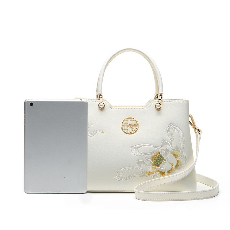 White handbag with floral design and gold accents on a white background