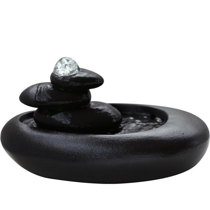 Black stone-like decorative item with a crystal on top on a white background
