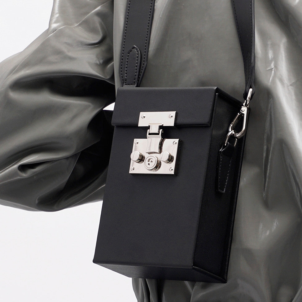 Black handbag with silver clasp on a gray raincoat background