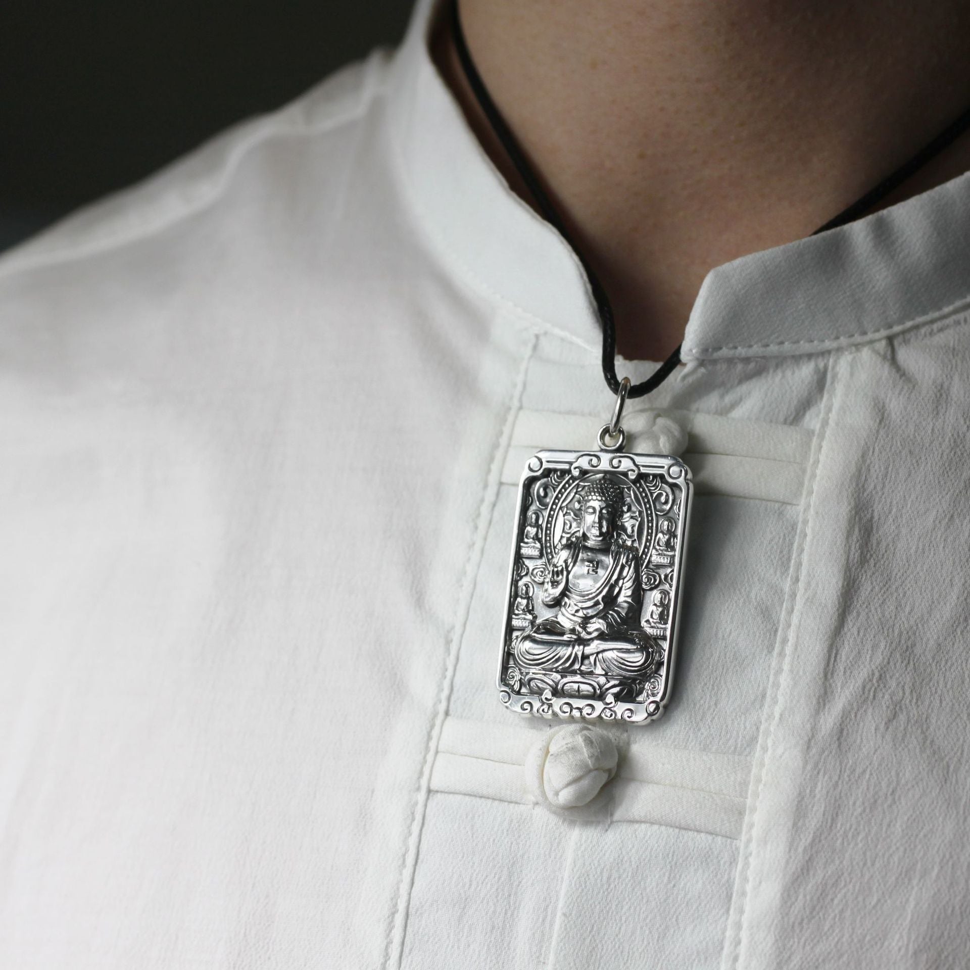 Silver pendant on a black cord worn by a person in a white shirt.
