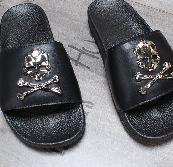 Black slides with gold skull and crossbones design on a gray surface