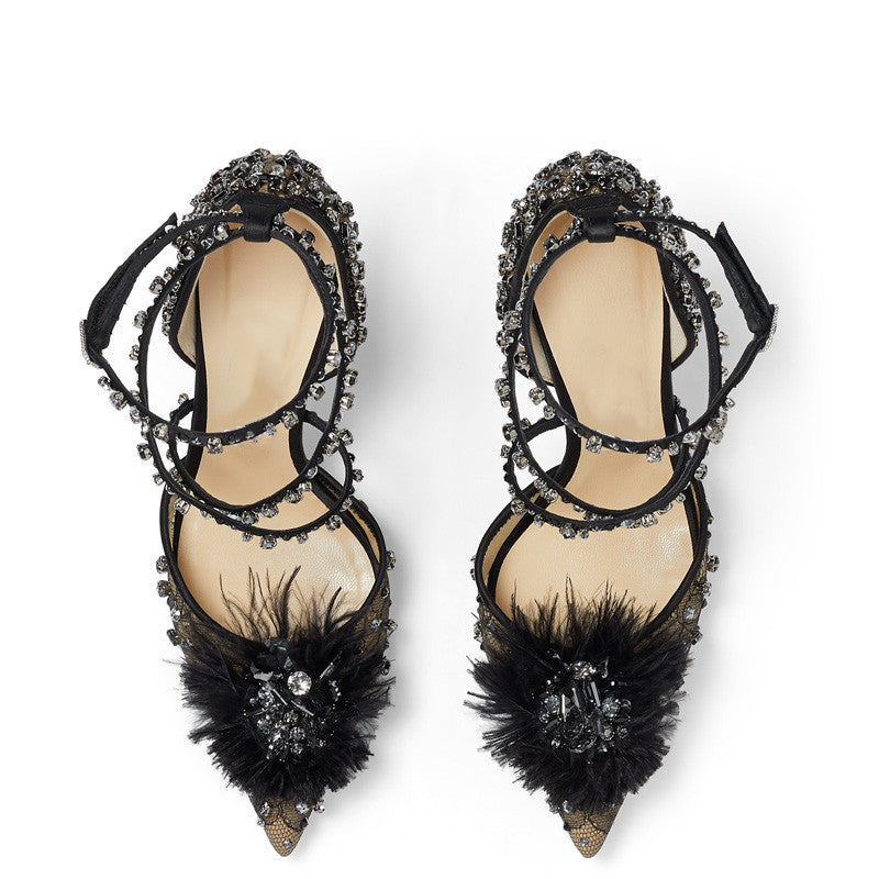Black high-heeled shoes with feather details and crystal embellishments on a white background