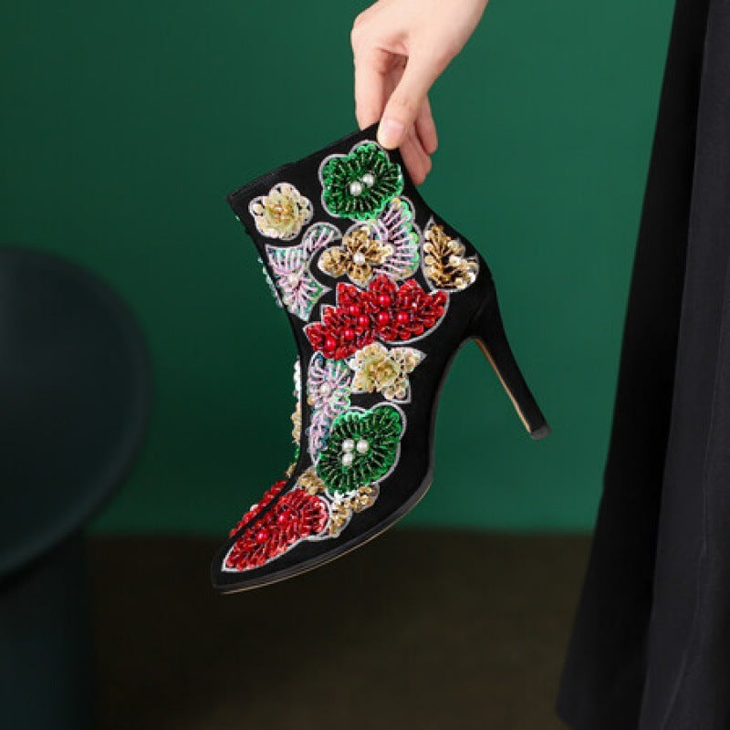 Black high-heeled shoe with colorful floral embroidery held against a green background