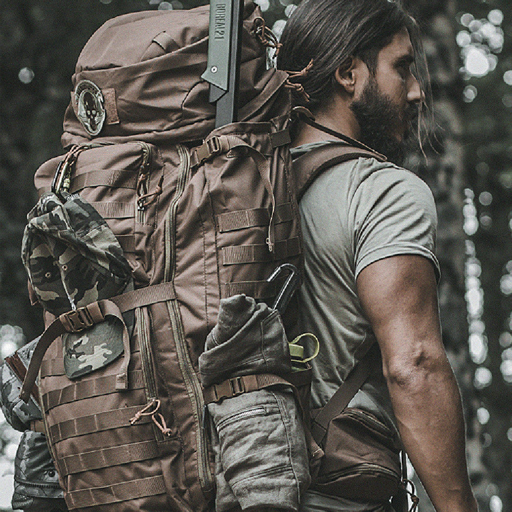 Person wearing a large brown backpack with tactical gear in a forest setting