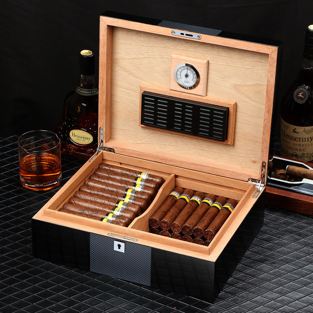 Wooden humidor with cigars, glass of whiskey, and bottles on a dark surface