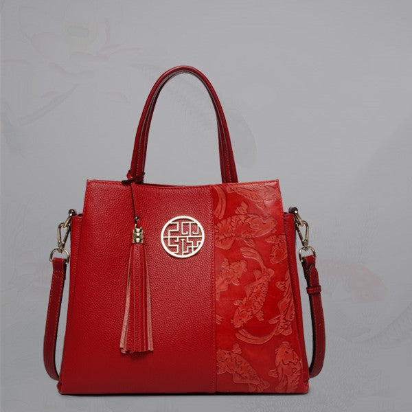 Red handbag with floral patterns and a gold emblem on a gray background
