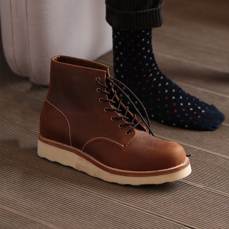 Brown leather boot on a wooden floor with a person wearing dark socks with colorful patterns.