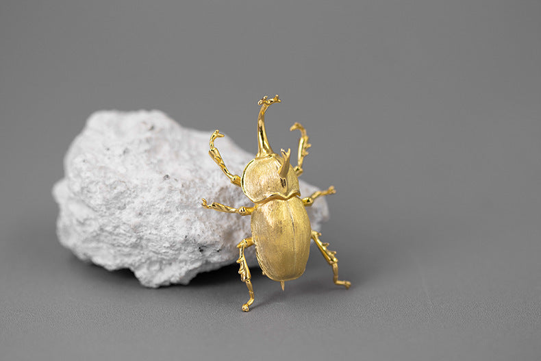 Gold beetle figurine on a gray surface with a gray background