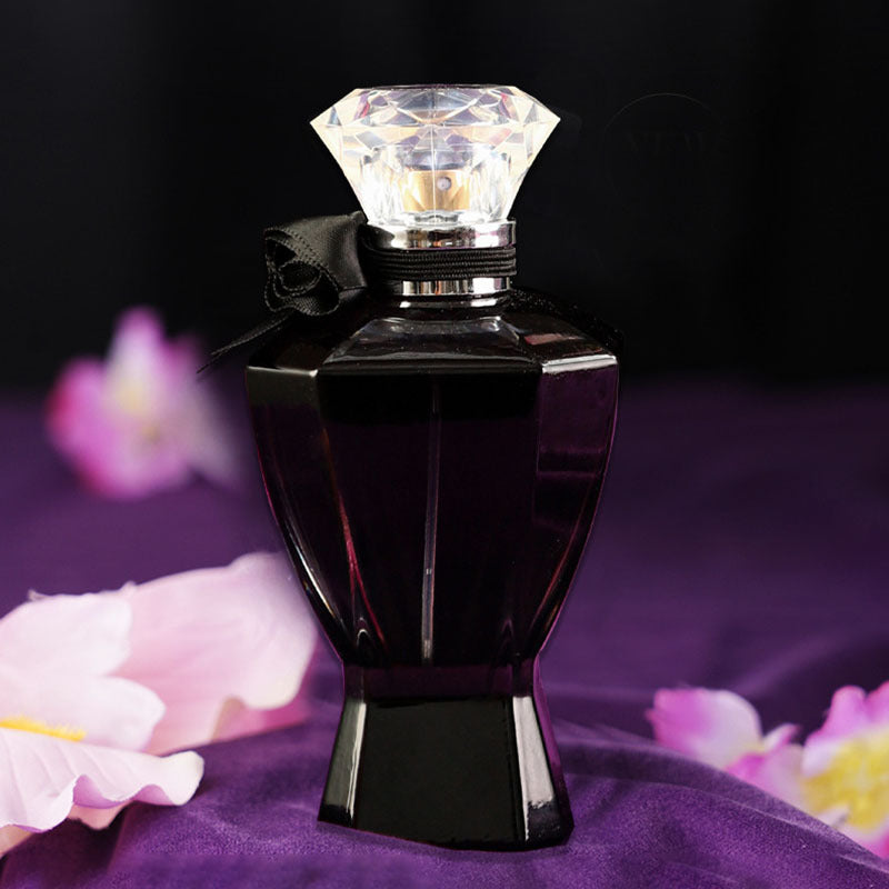 Black perfume bottle with a diamond-shaped cap on a purple fabric background with flowers.