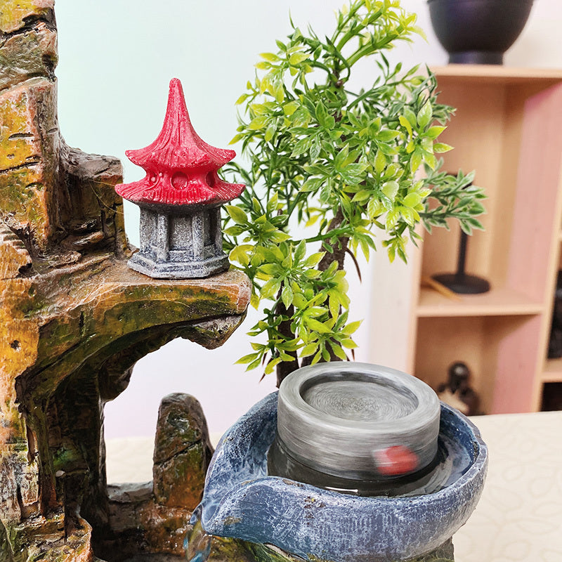 Decorative miniature pagoda with a red roof on a stone base next to a small potted plant.