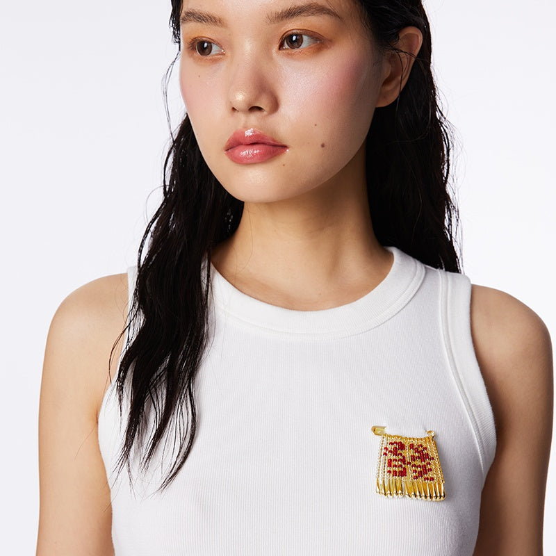 Woman wearing a white sleeveless top with a decorative brooch on a plain background
