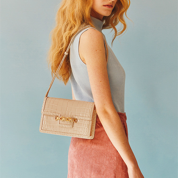 Woman holding a beige handbag with a gold chain strap against a light blue background