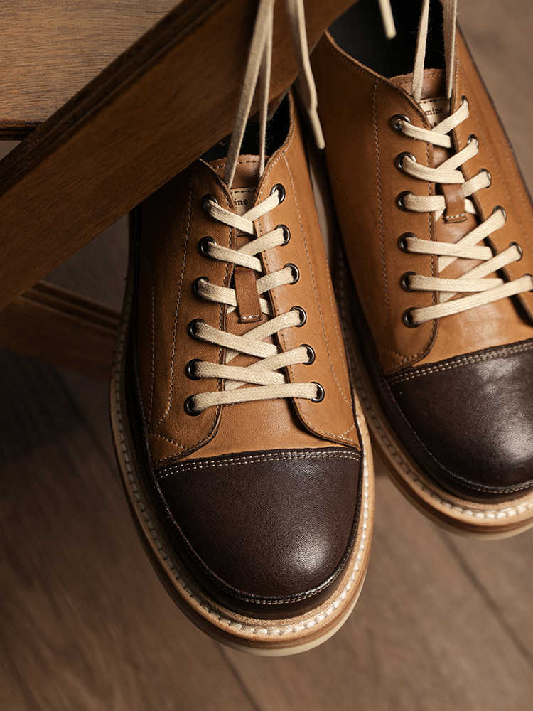 Pair of brown and black leather shoes with white laces on a wooden surface.