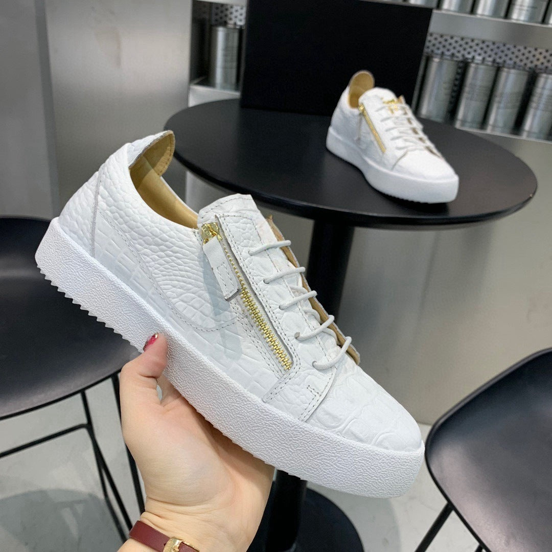 White sneakers with gold zippers held by a hand, with another pair in the background.