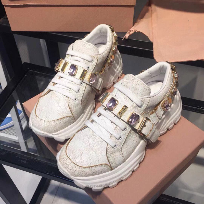 White sneakers with gold buckles and purple stones on a glass surface