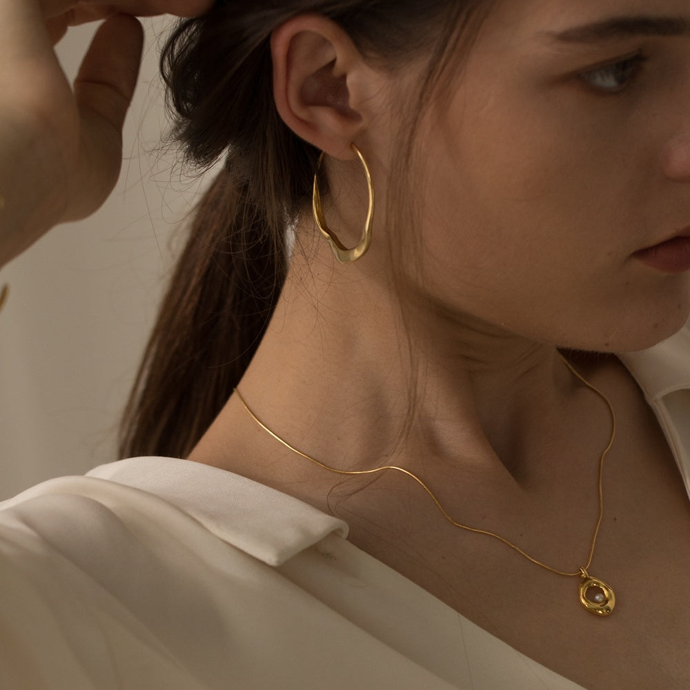Close-up of a person wearing gold hoop earrings and a necklace with a pendant.