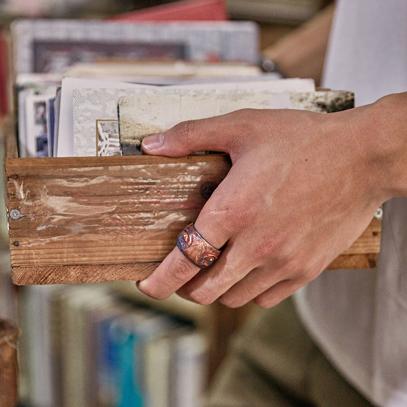 Hand holding a wooden box with books inside, blurred bookshelf in the background