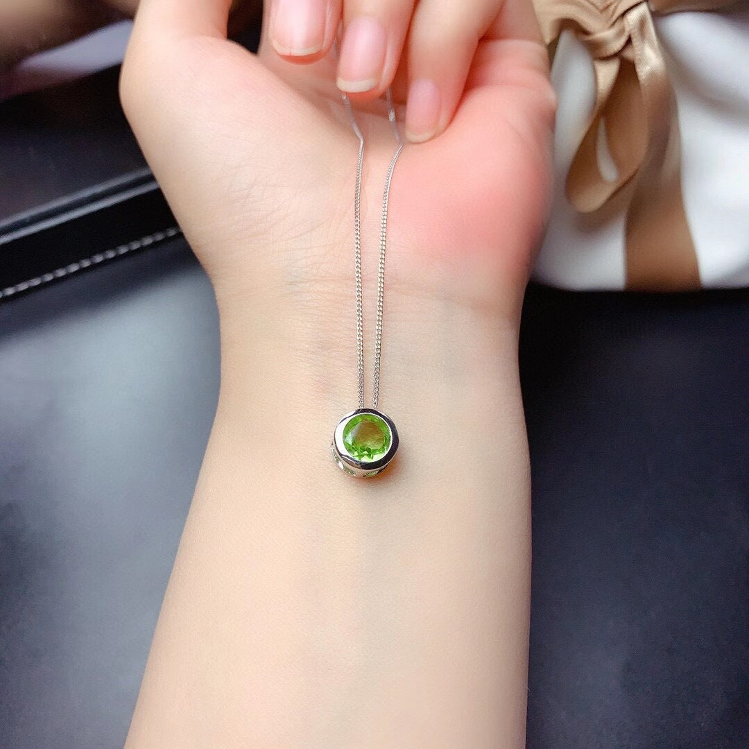 Necklace with a green pendant on a wrist against a neutral background