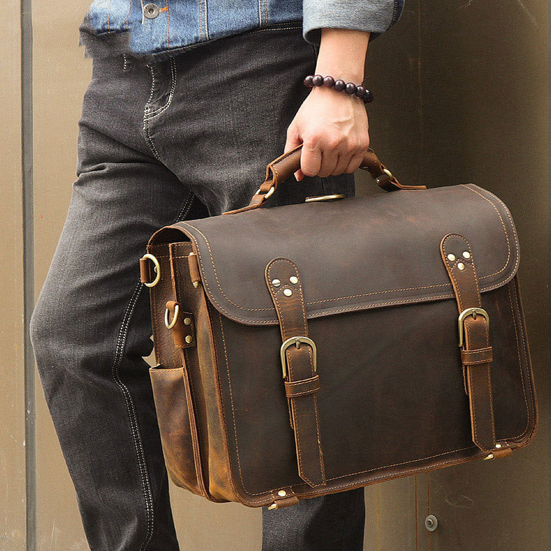 Person holding a brown leather briefcase against a neutral background