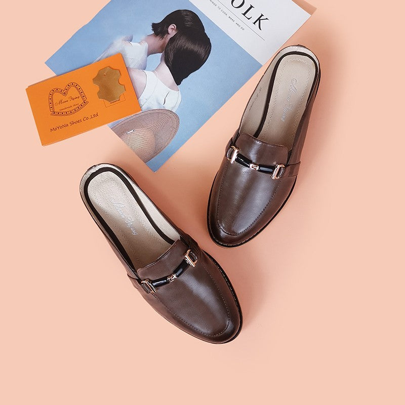 Brown loafers with gold buckles on a peach surface with a magazine and card.