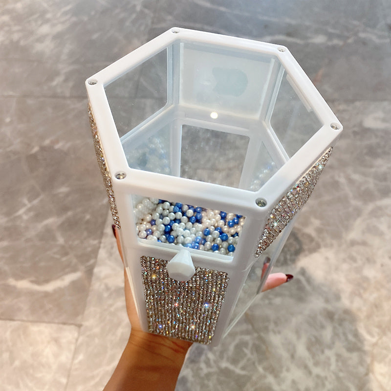 Hexagonal jewelry box with decorative elements held by a hand on a neutral background