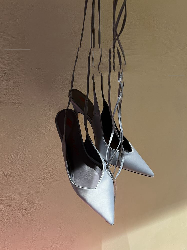 Pair of black high-heeled shoes with thin straps hanging against a beige background