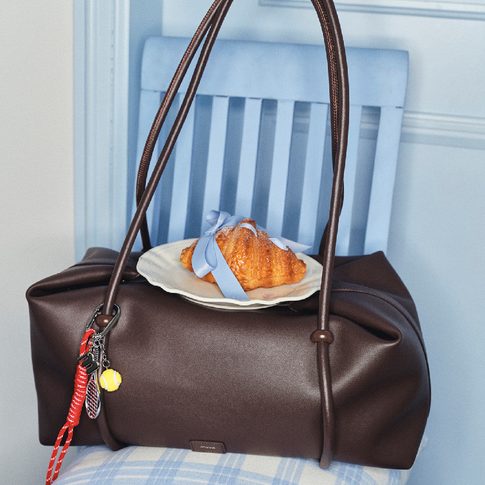 Brown handbag with a plate of croissant and blue ribbon on a chair