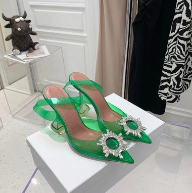 Green high-heeled shoes with embellishments on a white surface.