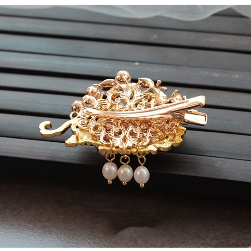 Gold hair clip with pearl decorations on a dark wooden surface