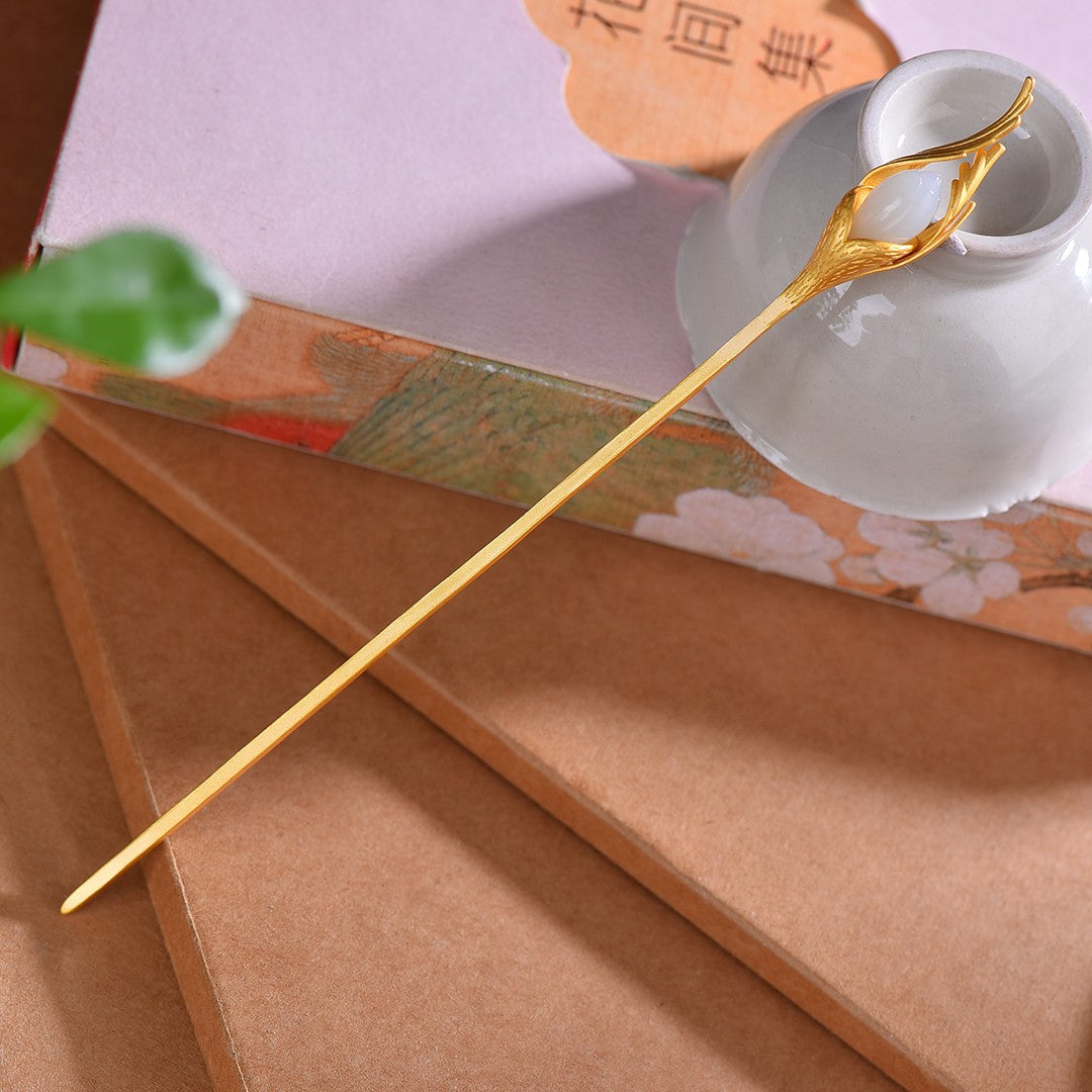Gold spoon with decorative handle on a brown surface with a white cup and pink book in the background.