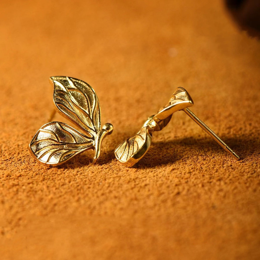 Gold leaf-shaped earrings on a textured orange surface