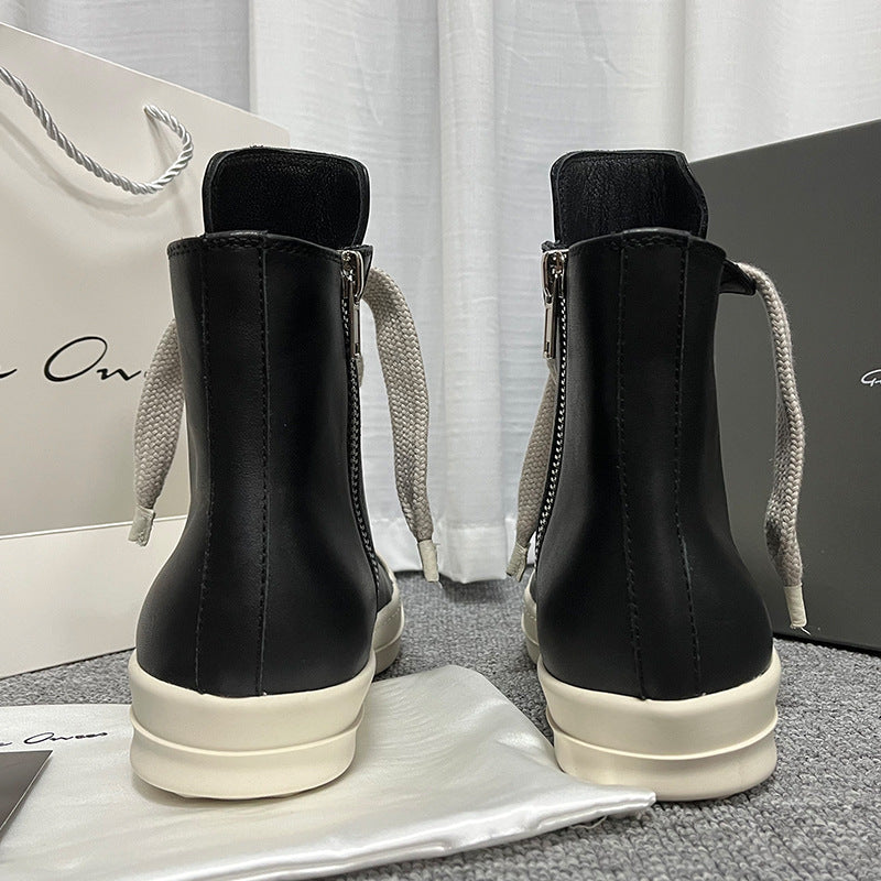 Black high-top sneakers with white soles on a gray surface with a white curtain background.