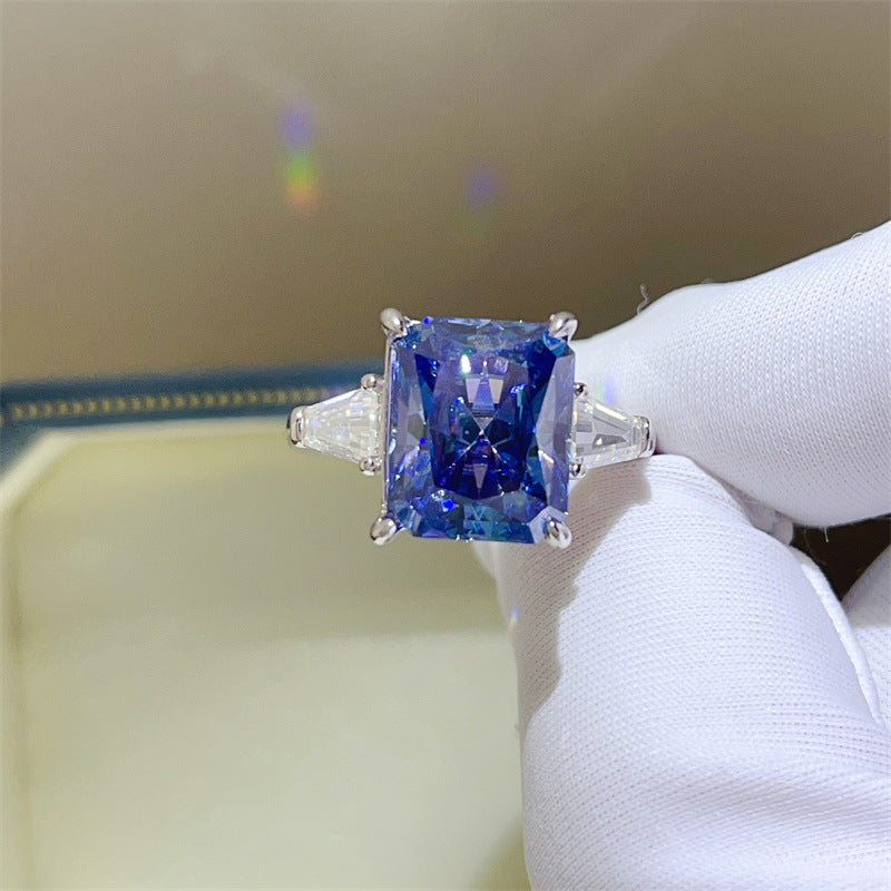 Blue gemstone ring held by a gloved hand against a neutral background
