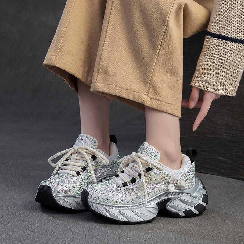 White sneakers with black soles worn by a person in a beige outfit on a dark background
