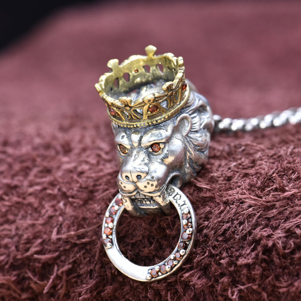 Silver lion head pendant with a gold crown on a brown textured background