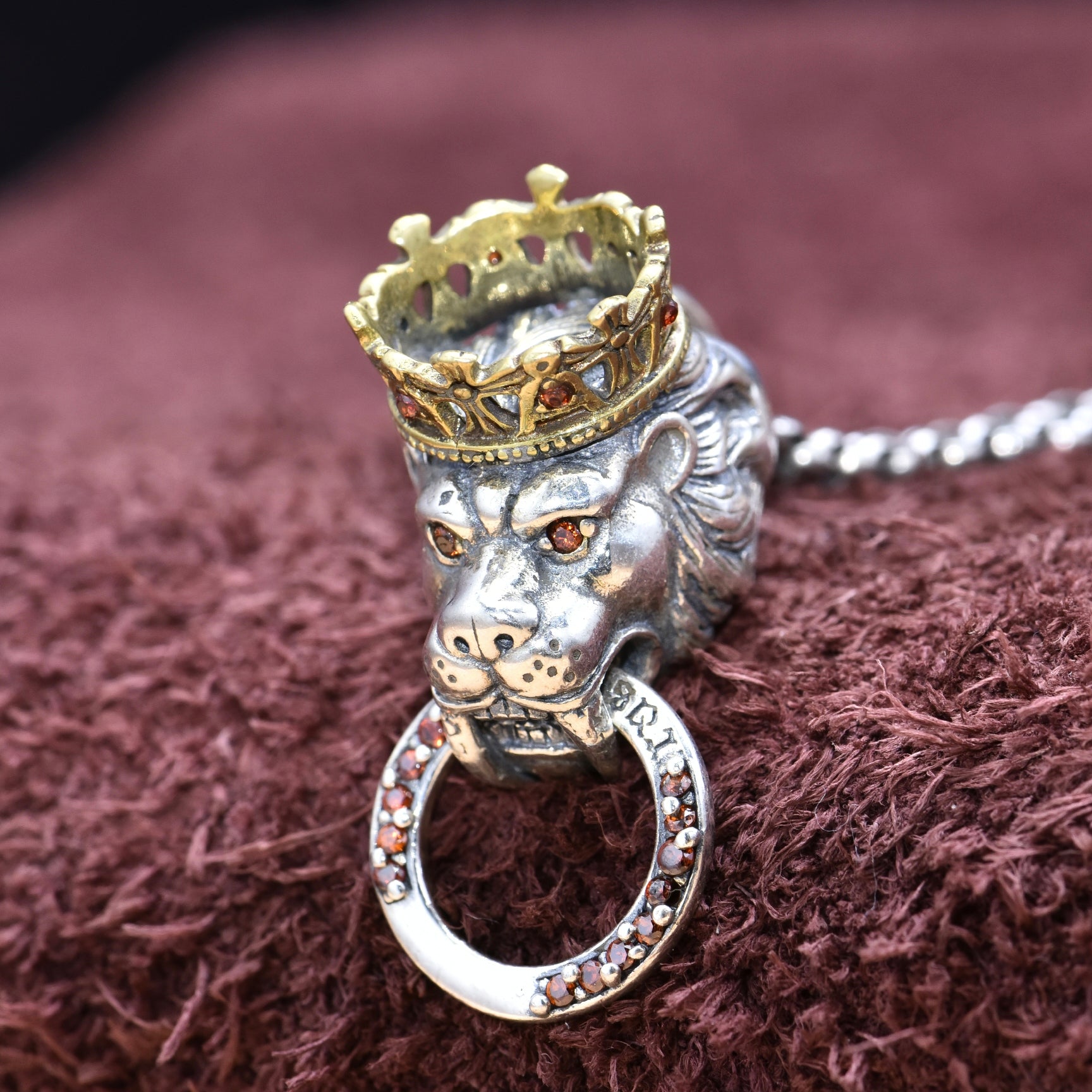Silver lion head pendant with a gold crown on a brown textured background