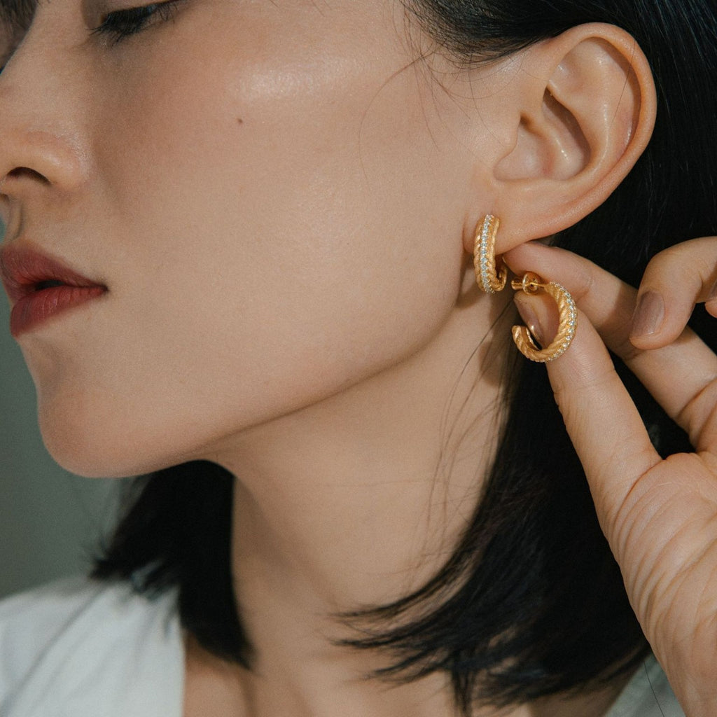 Close-up of a person wearing gold hoop earrings with a neutral background