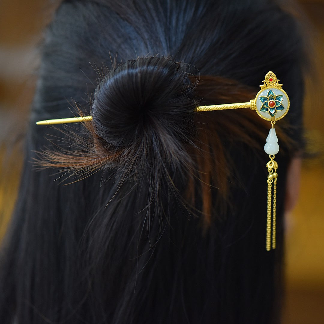 Decorative hairpin with gold tassel and green gemstone on a blurred background
