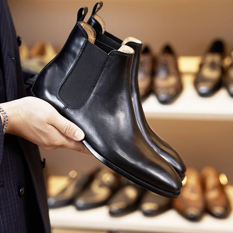 Person holding a black leather boot with shoes displayed in the background