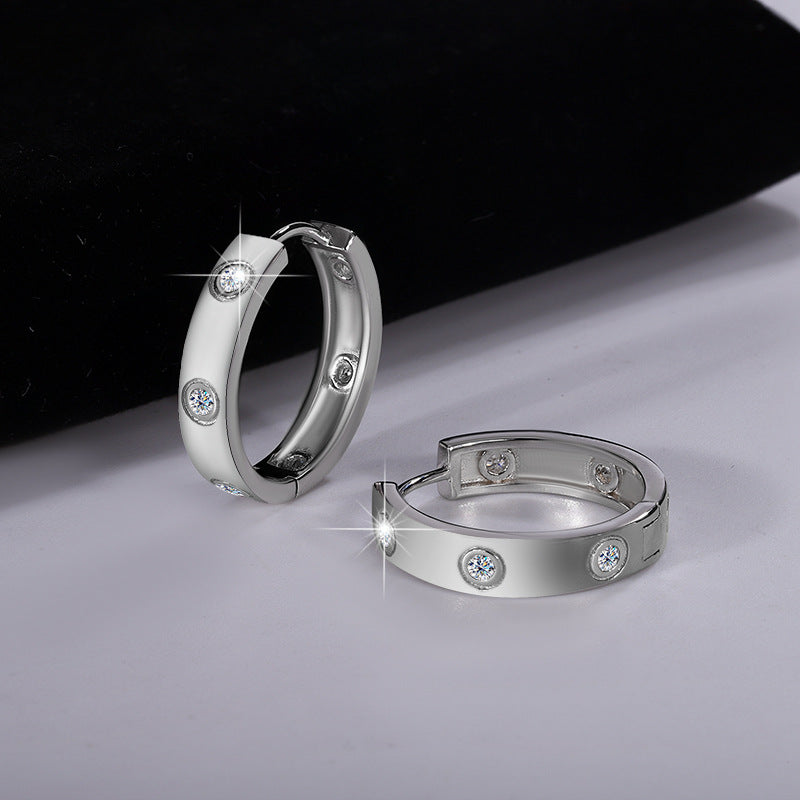 Pair of silver hoop earrings with embedded diamonds on a reflective surface.