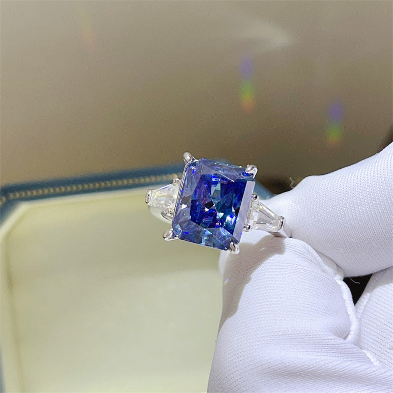 Ring with a blue gemstone held by a gloved hand against a neutral background