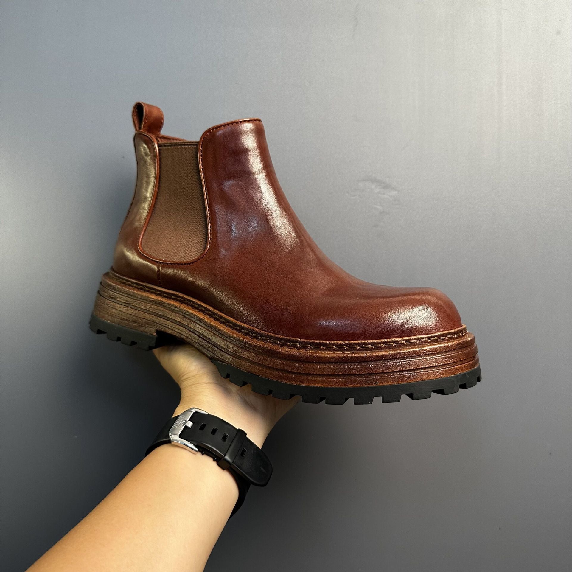 Brown leather boot held by a hand against a gray background
